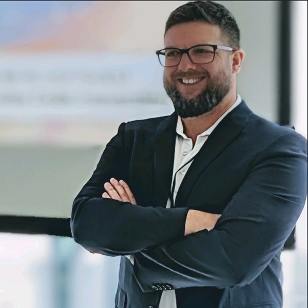 Brian Baldock, bearded and wearing glasses and a dark blazer, smiling with arms crossed.